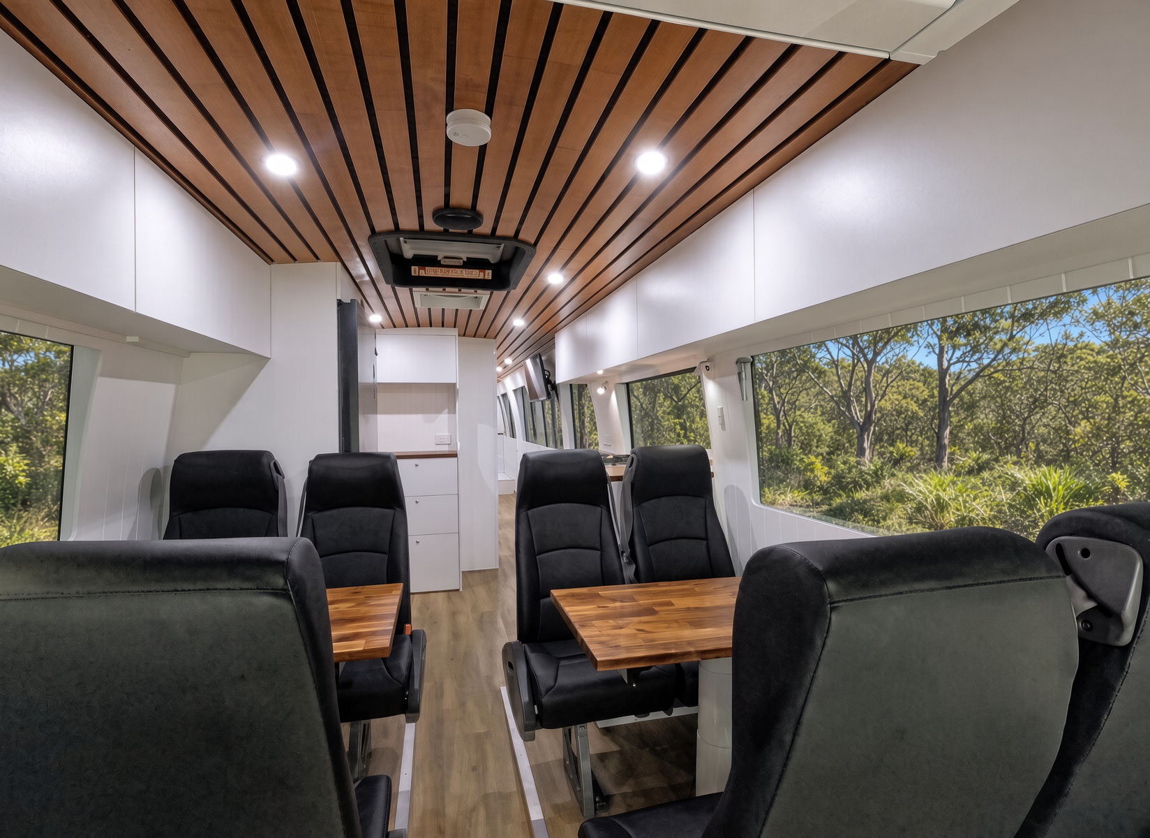 Campervan interior with wood tables, captain chairs and slat ceiling.